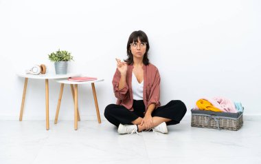 Genç melez kadın, katlanan giysiler, beyaz arka planda izole bir şekilde oturuyor, dua ediyor ve en iyisini diliyor.