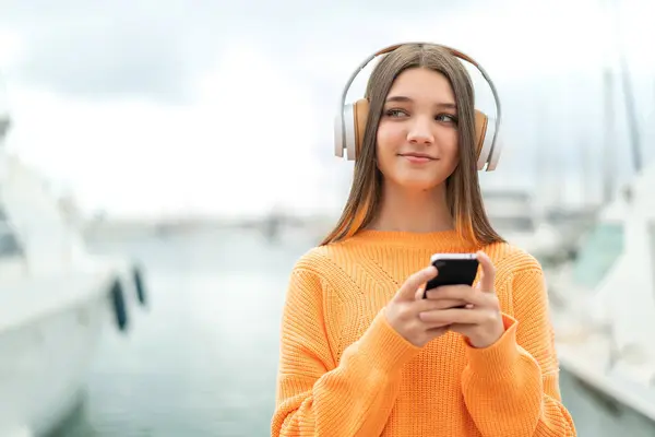 モバイルと思考で音楽を聞くアウトドアのティーンエイジャーガール — ストック写真