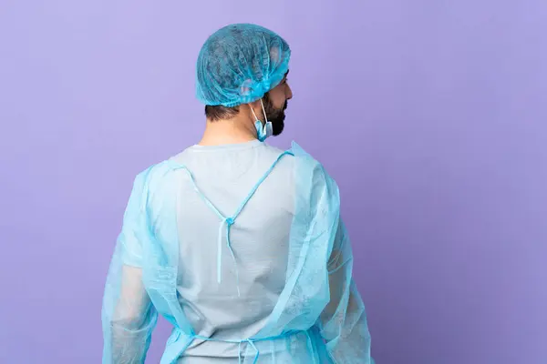 Хирург Бородой Синей Форме Изолированном Фиолетовом Фоне Задней Позиции Смотрящей — стоковое фото