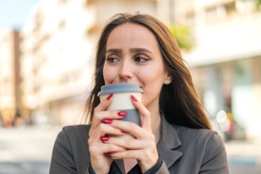 Açık havada elinde kahve tutan genç bir kadın.
