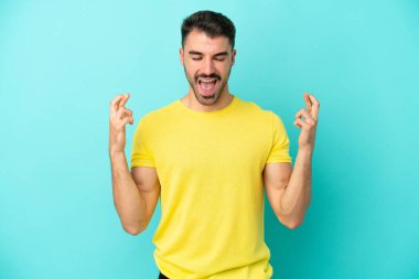 Genç beyaz adam mavi arka planda izole edilmiş ve şans diliyor.