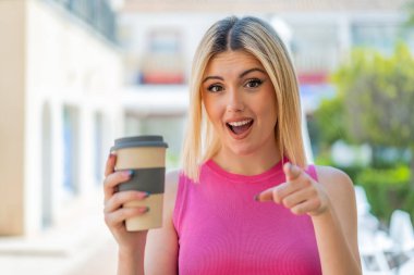 Genç, güzel sarışın kadın açık havada şaşırmış ve ön tarafı işaret ediyor.