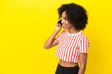 Sarı arka planda izole edilmiş genç Afrikalı Amerikalı kadın cep telefonuyla sohbet ediyor.
