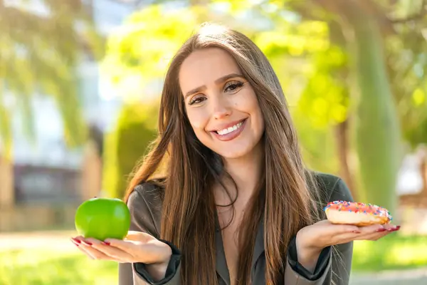Młoda Kobieta Świeżym Powietrzu Trzyma Jabłko Pączka Szczęśliwym Wyrazem Twarzy — Zdjęcie stockowe