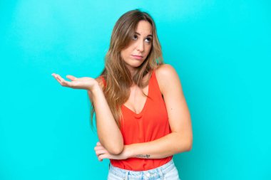 Kafkasyalı genç bir kadın mavi arka planda izole edilmiş. Şüpheleri var.