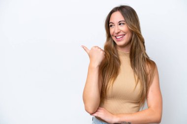 Beyaz arka planda izole edilmiş genç beyaz kadın bir ürünü sunmak için kenarı işaret ediyor.