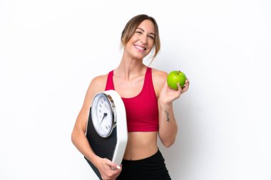 Beyaz arka planda, tartı makinesi ve elmasıyla izole edilmiş genç beyaz bir kadın.