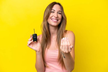 Sarı arka planda izole edilmiş araba anahtarlarını tutan beyaz bir kadın... -... benimle gelmesi için davet ediyor. Gelmene sevindim.