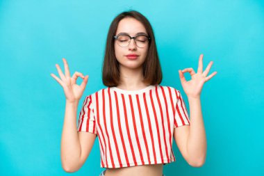 Genç Ukraynalı kadın Zen pozunda mavi arka planda izole edilmiş.