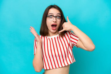 Mavi arka planda izole edilmiş genç Ukraynalı bir kadın telefon hareketinde bulunuyor.