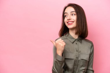 Pembe arka planda izole edilmiş genç Ukraynalı kadın bir ürünü sunmak için kenarı işaret ediyor.