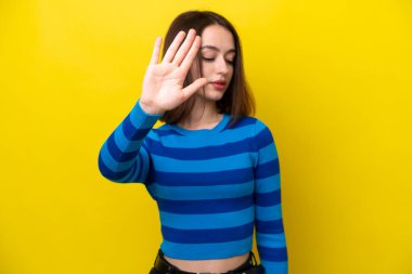 Sarı arka planda izole edilmiş genç Ukraynalı kadın dur hareketi yapıyor ve hayal kırıklığına uğruyor