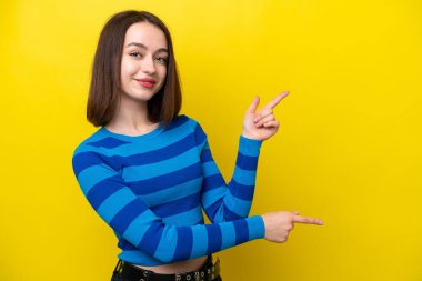 Sarı arka planda izole edilmiş genç Ukraynalı bir kadın parmak göstererek bir ürün sunuyor.