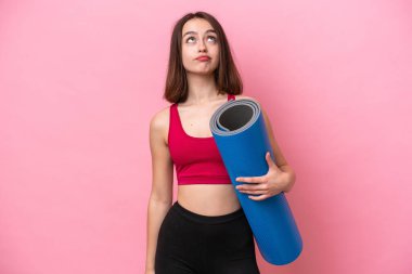 Genç sporcu Ukraynalı kadın yoga derslerine giderken elinde pembe arka planda izole edilmiş bir minder tutarak yukarı bakıyor.