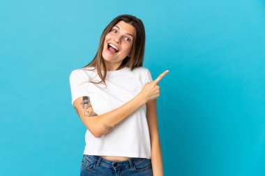 Mavi arka planda izole edilmiş genç Slovak kadın şaşırmış ve işaret ediyor.