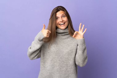 Mor arka planda izole edilmiş genç Slovak kadın işaret ve baş parmak hareketi gösteriyor