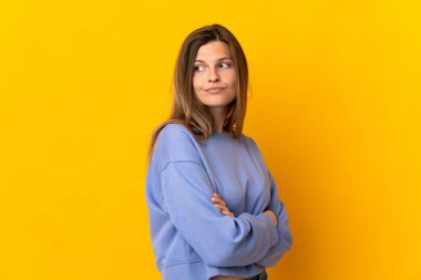 Sarı arka planda izole edilmiş genç Slovak kadın kollarını kavuşturuyor.