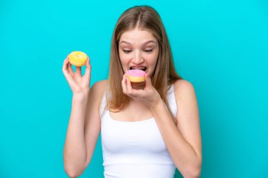 Genç Rus kız mavi arka planda izole edilmiş ve donut yiyor.