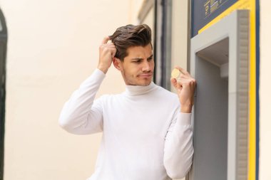 Açık havada ATM kullanan genç beyaz bir adam.
