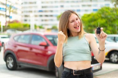 Açık havada araba anahtarı tutan genç sarışın kadın zaferi kutluyor.