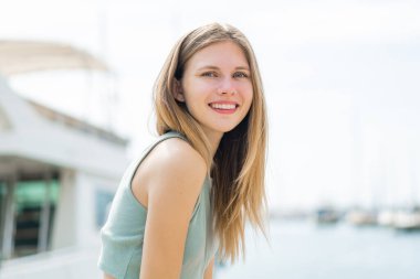 Açık havada genç sarışın bir kadın Neşeli bir ifadeyle