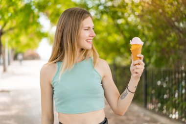 Genç, sarışın, güzel bir kadın. Açık havada kornet dondurması ve mutlu bir ifadesi var.