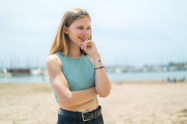 Açık havada genç sarışın kadın yan tarafa bakıyor.