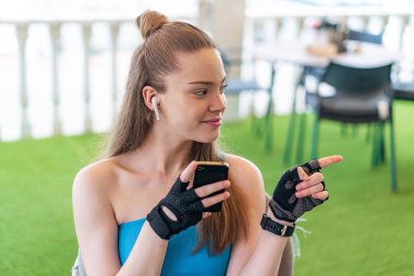 Açık havada cep telefonu kullanan genç ve güzel bir kız bir ürün sunmak için yan tarafı işaret ediyor.