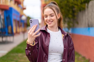 Dışarıda cep telefonu kullanan güzel bir kız. Mutlu bir ifadeyle.