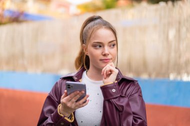 Deri ceketli bir kadın cep telefonuna bakıyor.