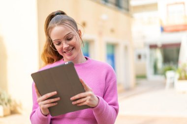 Açık havada elinde mutlu bir ifadeyle tablet tutan güzel bir kız.