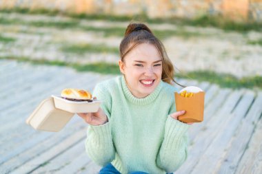 Dışarıdaki güzel kız elinde hamburger ve patates kızartması tutuyor.