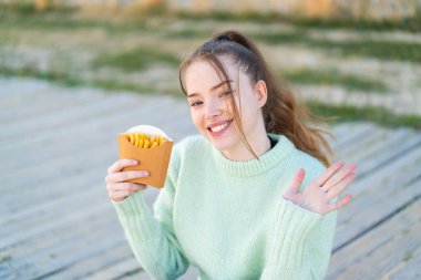 Dışarıda patates kızartması tutan genç ve güzel bir kız. Mutlu bir ifadeyle selamlıyor.