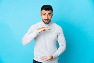 İzole edilmiş mavi arka plan üzerinde beyaz bir adam bir ilan vermek için avucunun içinde hayali bir mekan tutuyor.