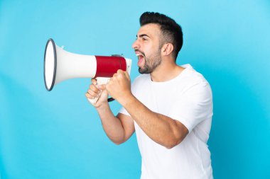 İzole edilmiş mavi arka plan üzerinde beyaz bir adam megafondan bir şey duyurmak için bağırıyor.
