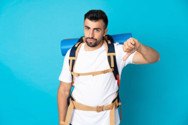 Genç dağcı mavi arkaplan üzerinde negatif ifade ile baş parmak aşağı gösteren