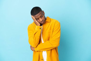 Mavi arka planda başağrısı olan genç Latin bir adam.