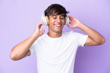 Young caucasian man isolated on purple background listening music and singing