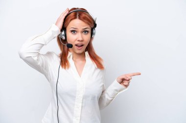 Beyaz arka planda izole edilmiş kulaklıkla çalışan pazarlamacı Rus kız şaşırmış ve parmağıyla kenarı işaret ediyor.