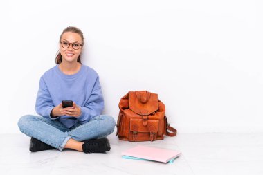 Beyaz arka planda izole bir katta oturan genç kız cep telefonuyla bir mesaj gönderiyor.