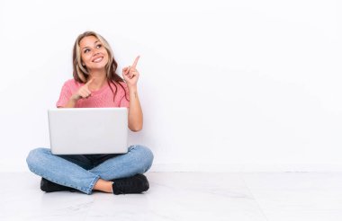 Yerde dizüstü bilgisayarı olan genç bir Rus kız beyaz arka planda izole edilmiş ve işaret parmağıyla işaret ediyor. Harika bir fikir.