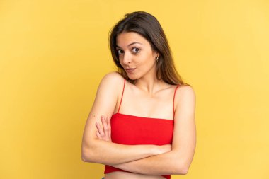 Sarı arka planda izole edilmiş genç, beyaz bir kadın omuzlarını kaldırırken şüpheyle hareket ediyor.