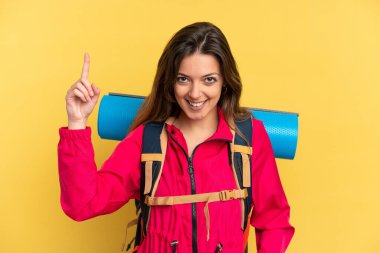 Young mountaineer man with a big backpack isolated on yellow background pointing up a great idea