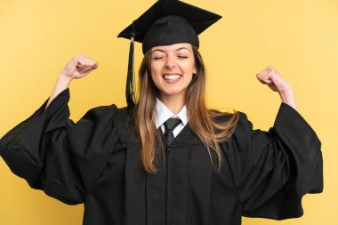 Sarı arka planda izole edilmiş genç üniversite mezunu güçlü bir jest yapıyor.