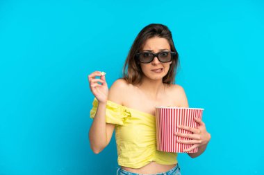 Mavi arka planda 3 boyutlu gözlüklü ve elinde koca bir kova patlamış mısır tutan beyaz bir kadın.