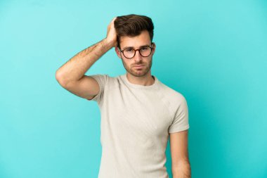 Kafkasyalı yakışıklı genç adam mavi arka planda izole edilmiş hayal kırıklığı ifadesi ve anlamama.