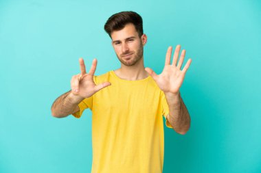 Beyaz tenli yakışıklı adam mavi arka planda izole edilmiş, parmaklarıyla sekizi sayıyor.