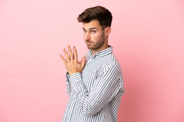 Beyaz tenli yakışıklı bir adam pembe arka planda izole edilmiş bir şeyler çeviriyor.