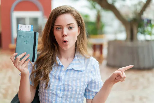 Young Redhead Woman Holding Passport Outdoors Surprised Pointing Side — Stock Photo, Image