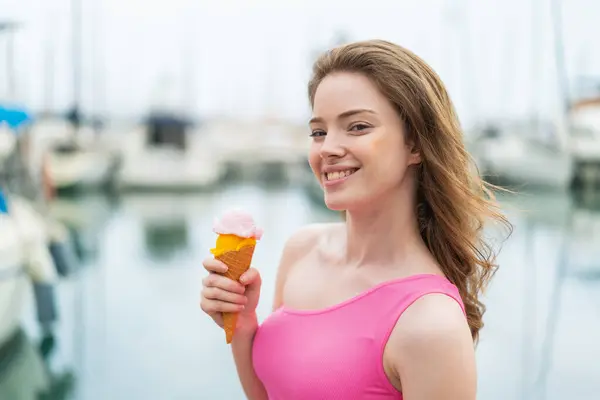 Young redhead woman with a cornet ice cream at outdoors smiling a lot